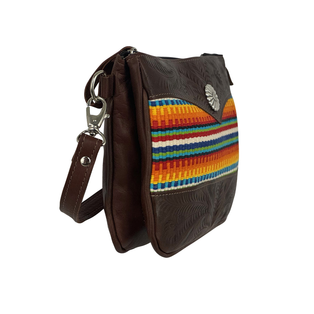 Side view of Maká Festive multi compartment crossbody in brown with hand tooled leather, red themed hand woven tapestry, and concho