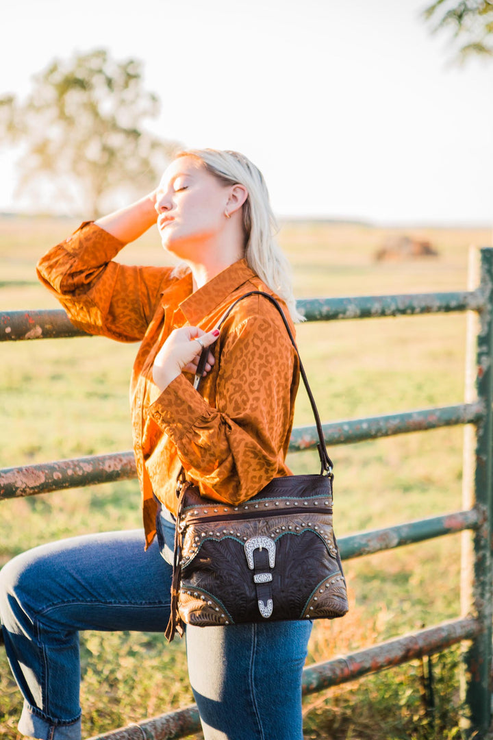 Lifestyle with model of Saddle Ridge shoulder bag in chocolate brown with hand tooled leather accents and buckle